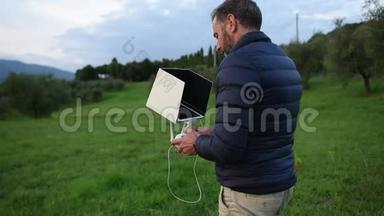 一个长胡子的男人穿着羽绒服，看着他的平板电脑，一边微笑着在田野里驾驶无人机